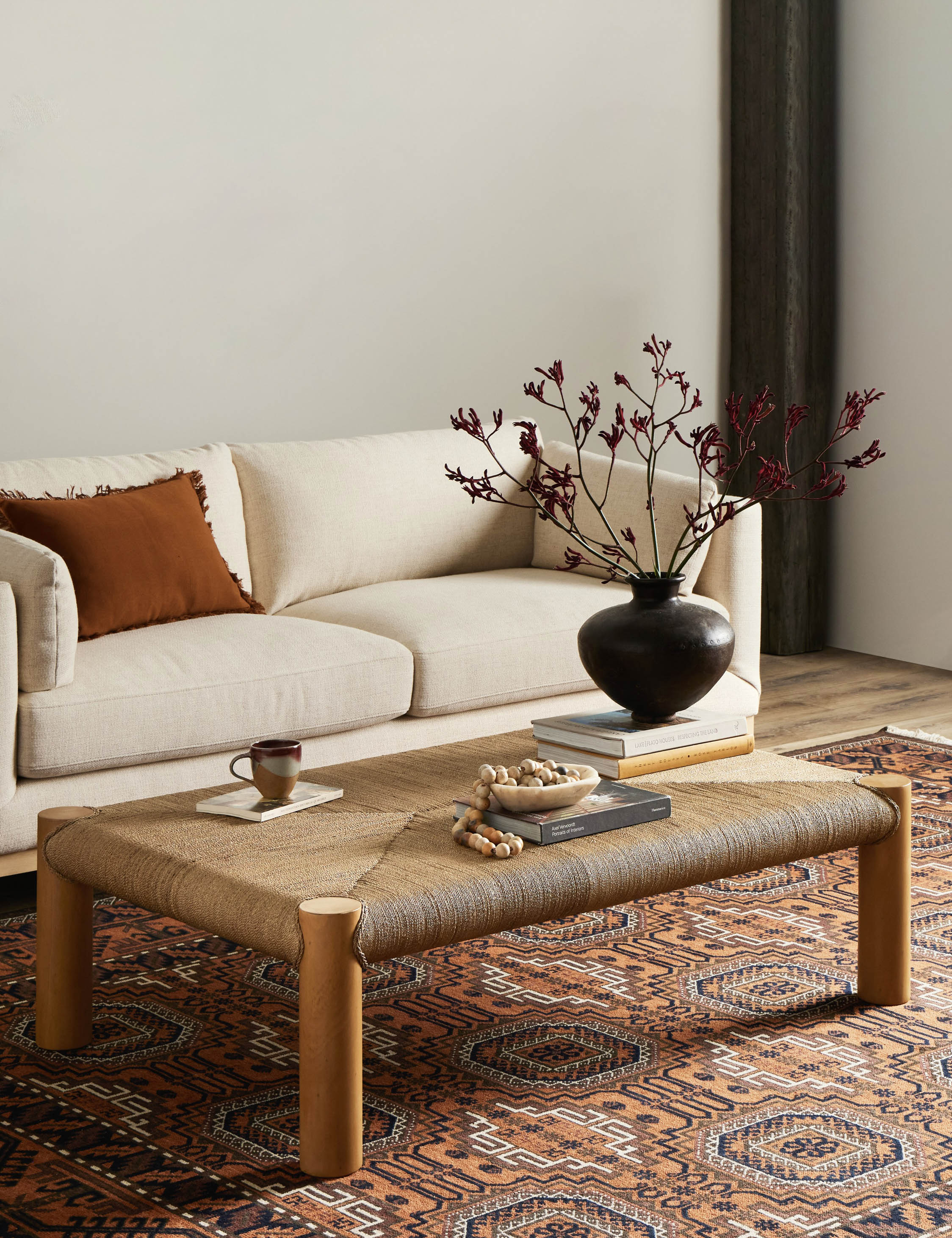 Lerner mahogany wood woven top coffee table styled with a cream colored sofa and orange geometric pattern area rug.
