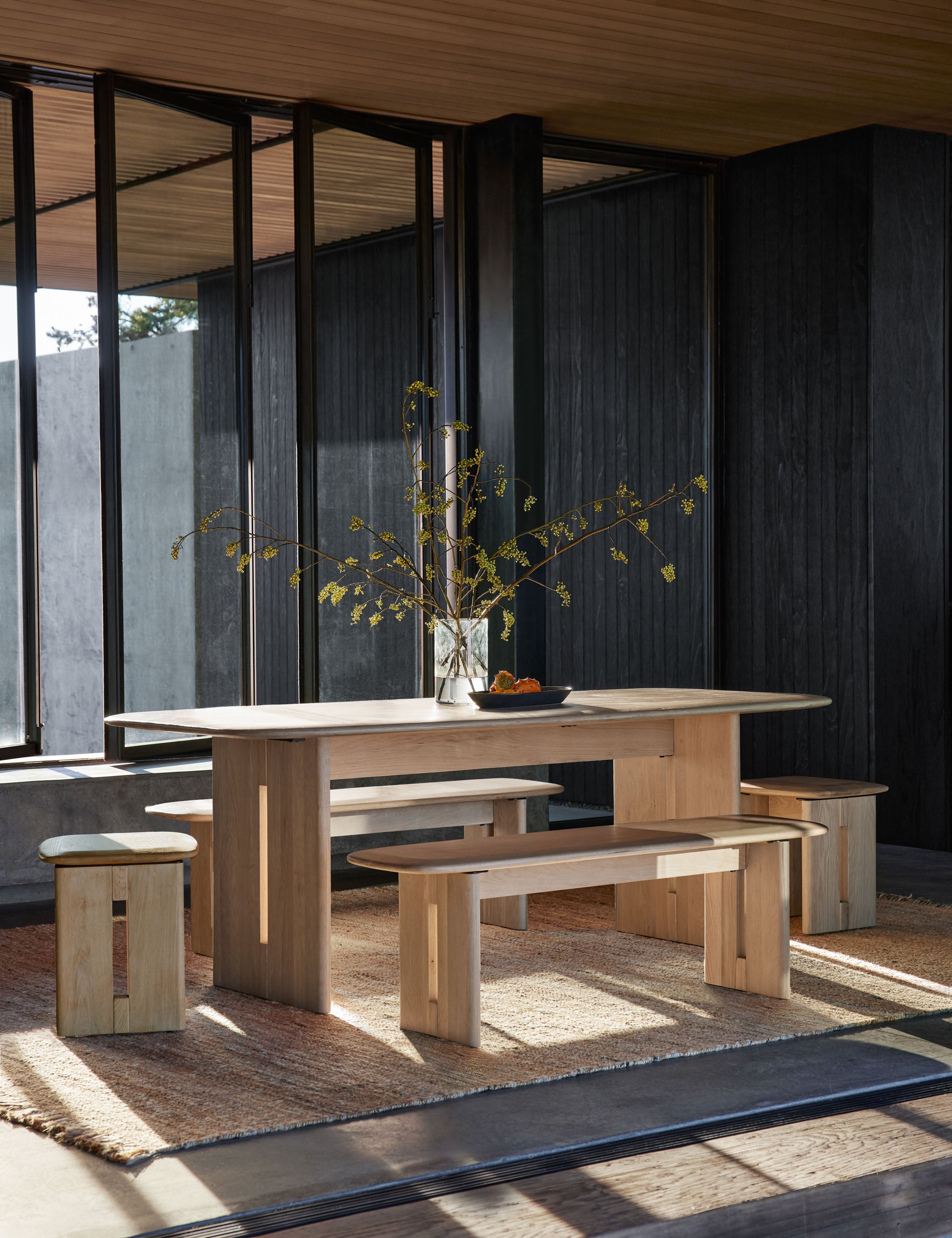 The Henrik light wood dining table sits atop a jute rug surrounded by the Henrik bench and Henrik side table