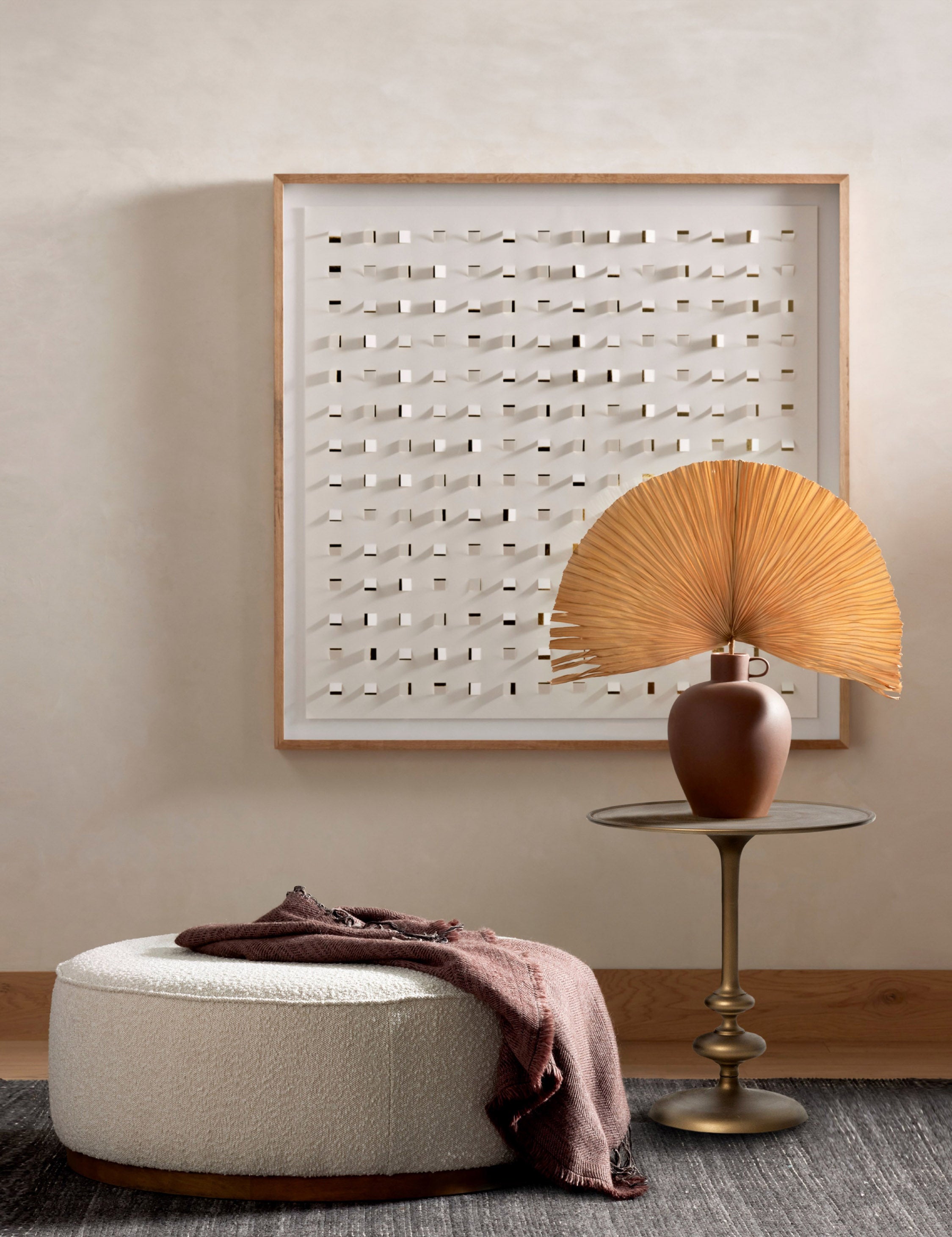 Caratto round matte brass finish metal side table styled next to a large round ottoman and modern wall artwork.