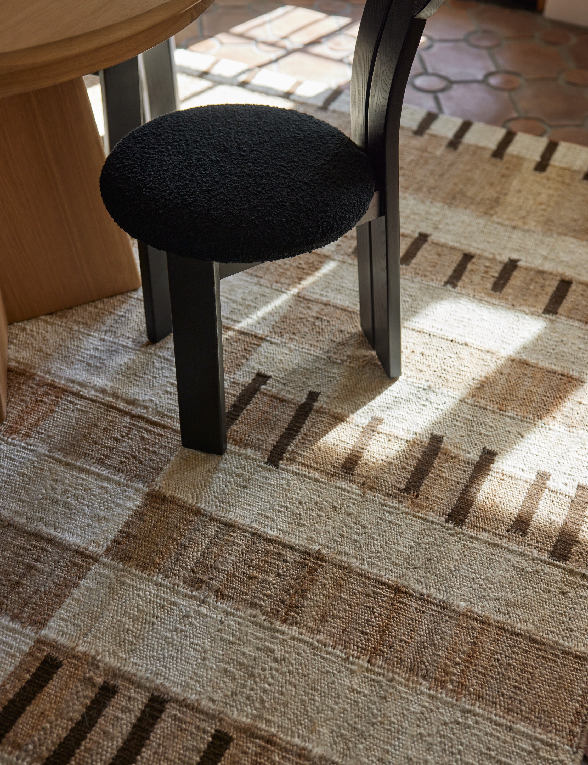 Tempo Flatweave Jute Rug by Elan Byrd under a black dining chair.