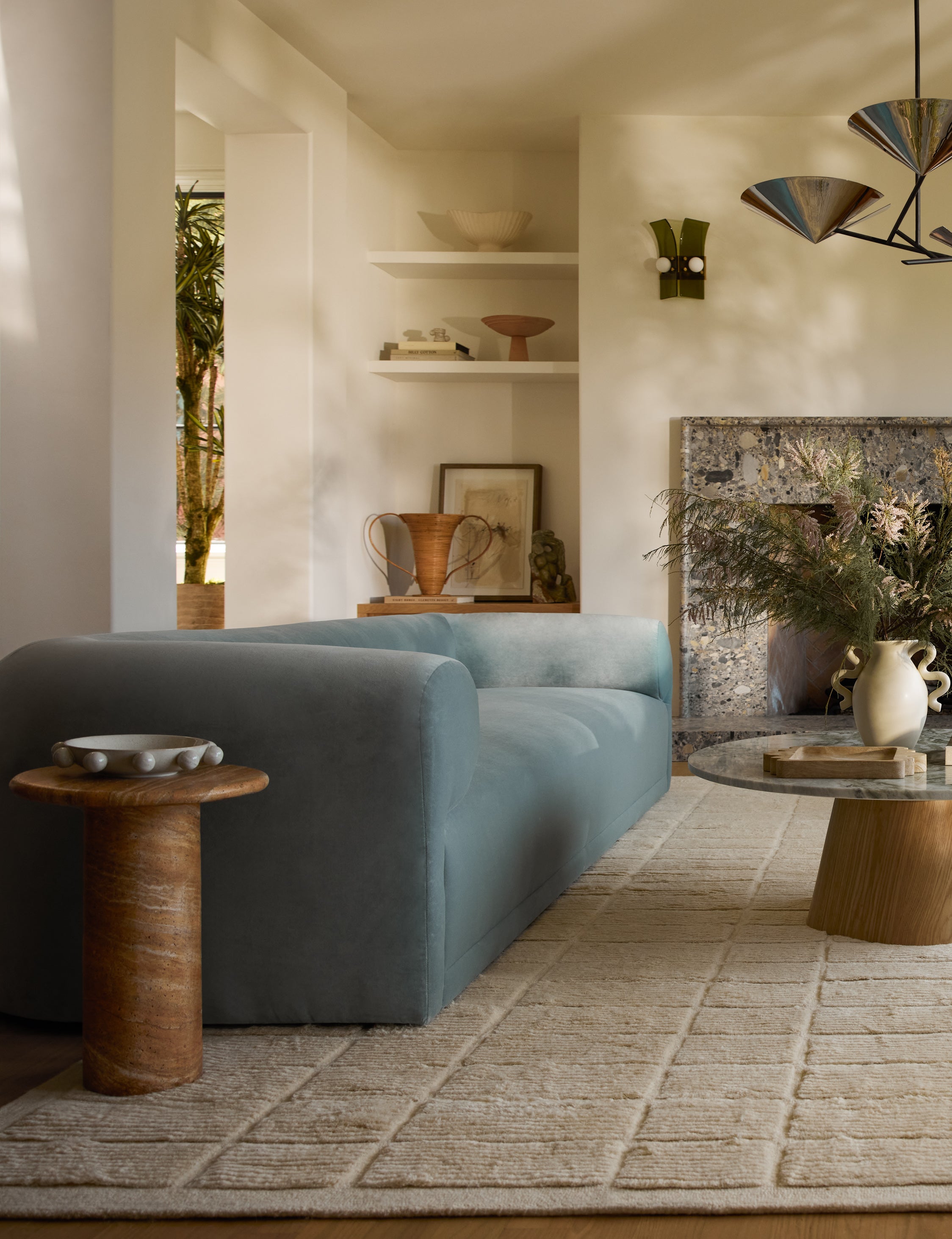 Mona round stone drink table styled next to a blue velvet sofa.