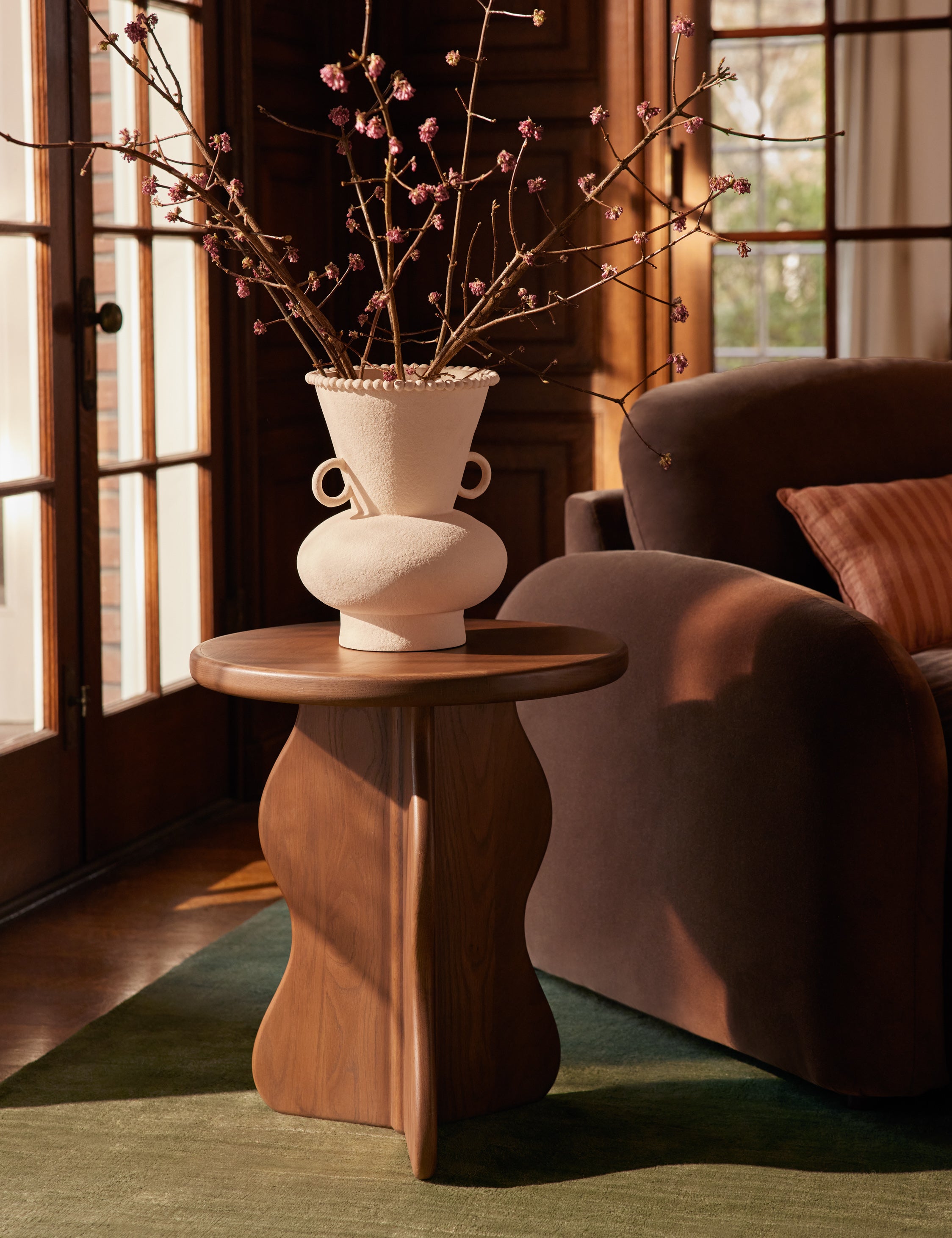 The Telle wavy leg solid wood round side table by Aimee Song with a ceramic vase on top styled next to an accent chair