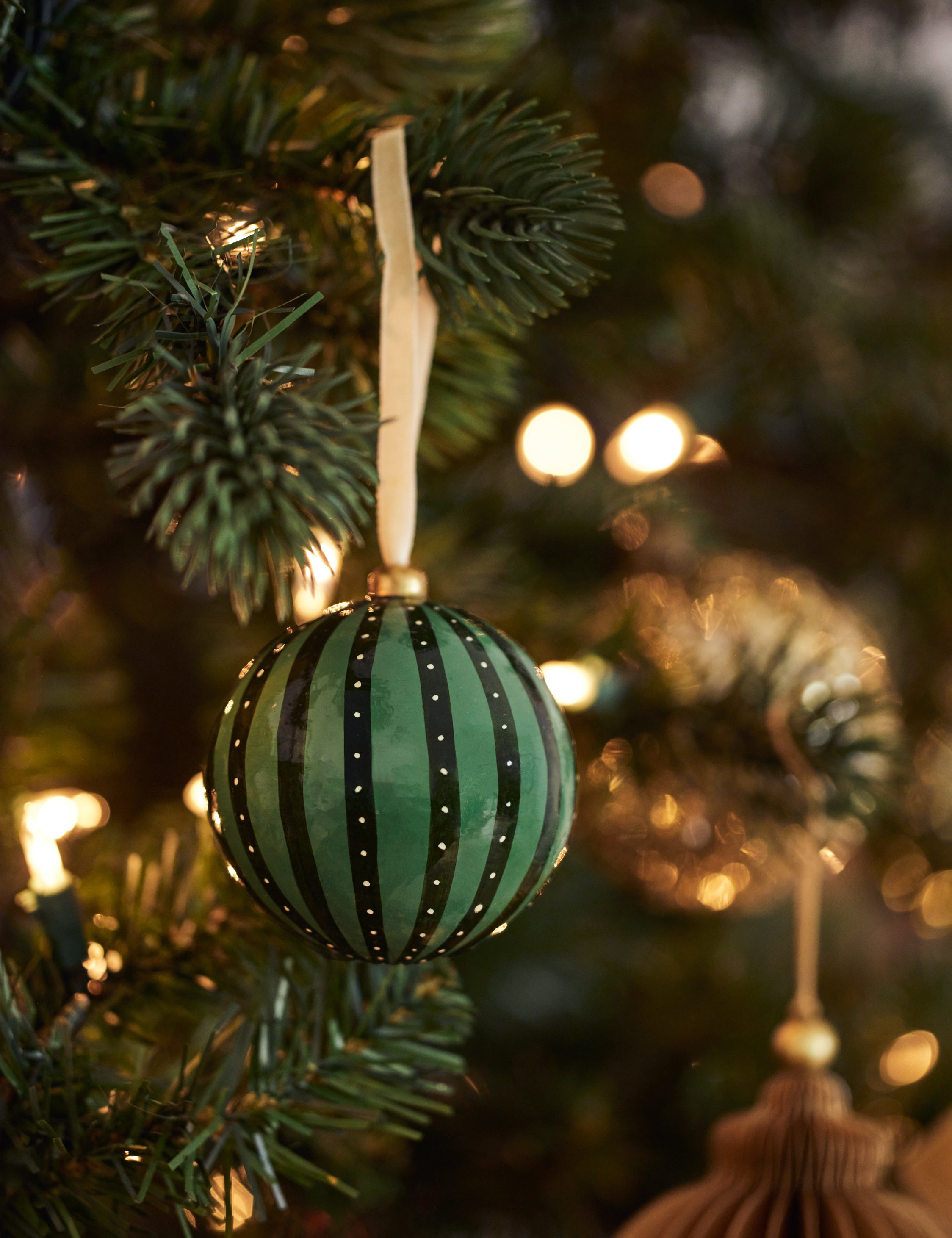 Joelle paper mache ornament hanging on a christmas tree branch