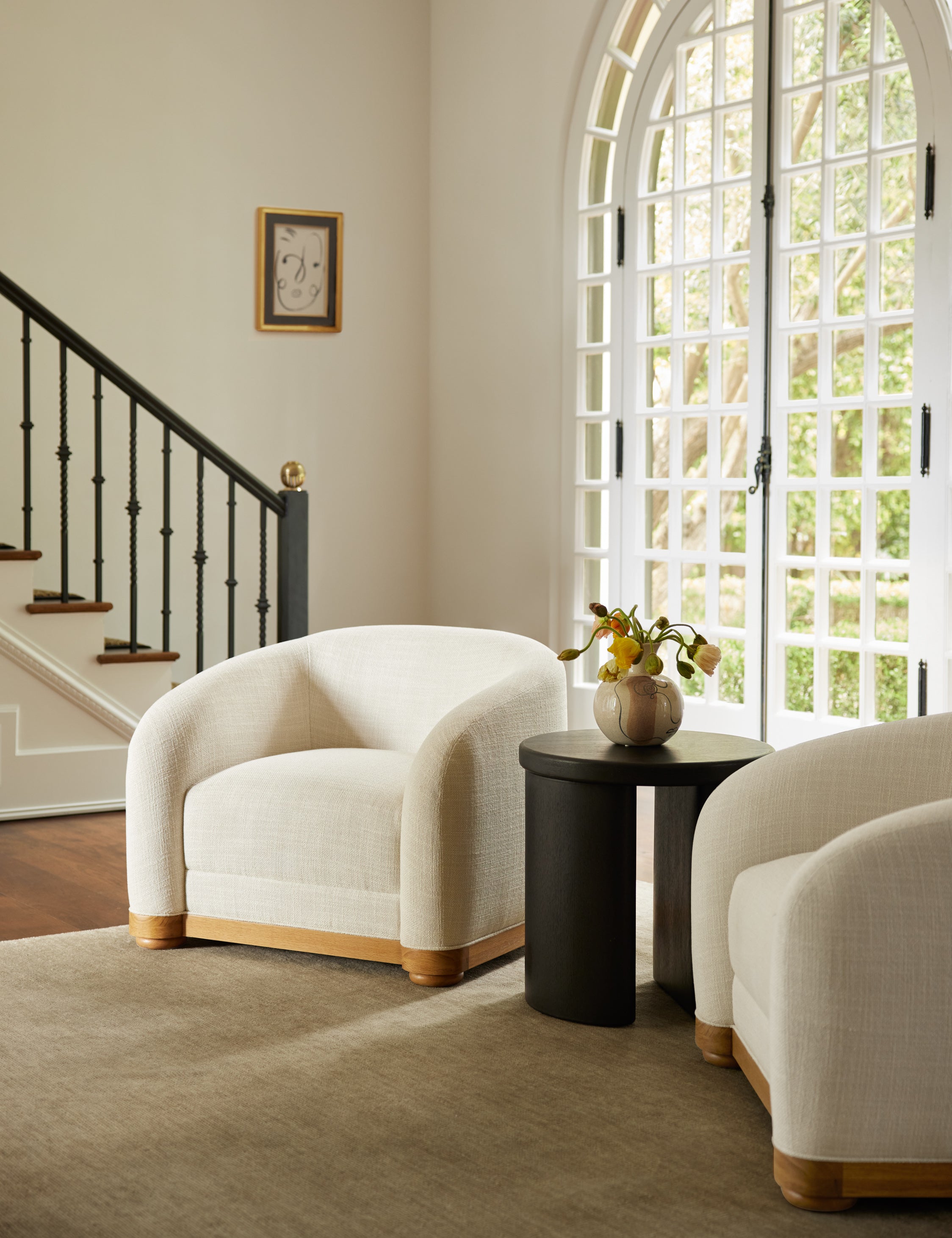 Two Marci low barrel accent chairs paired with the Olga round modern black oak side table