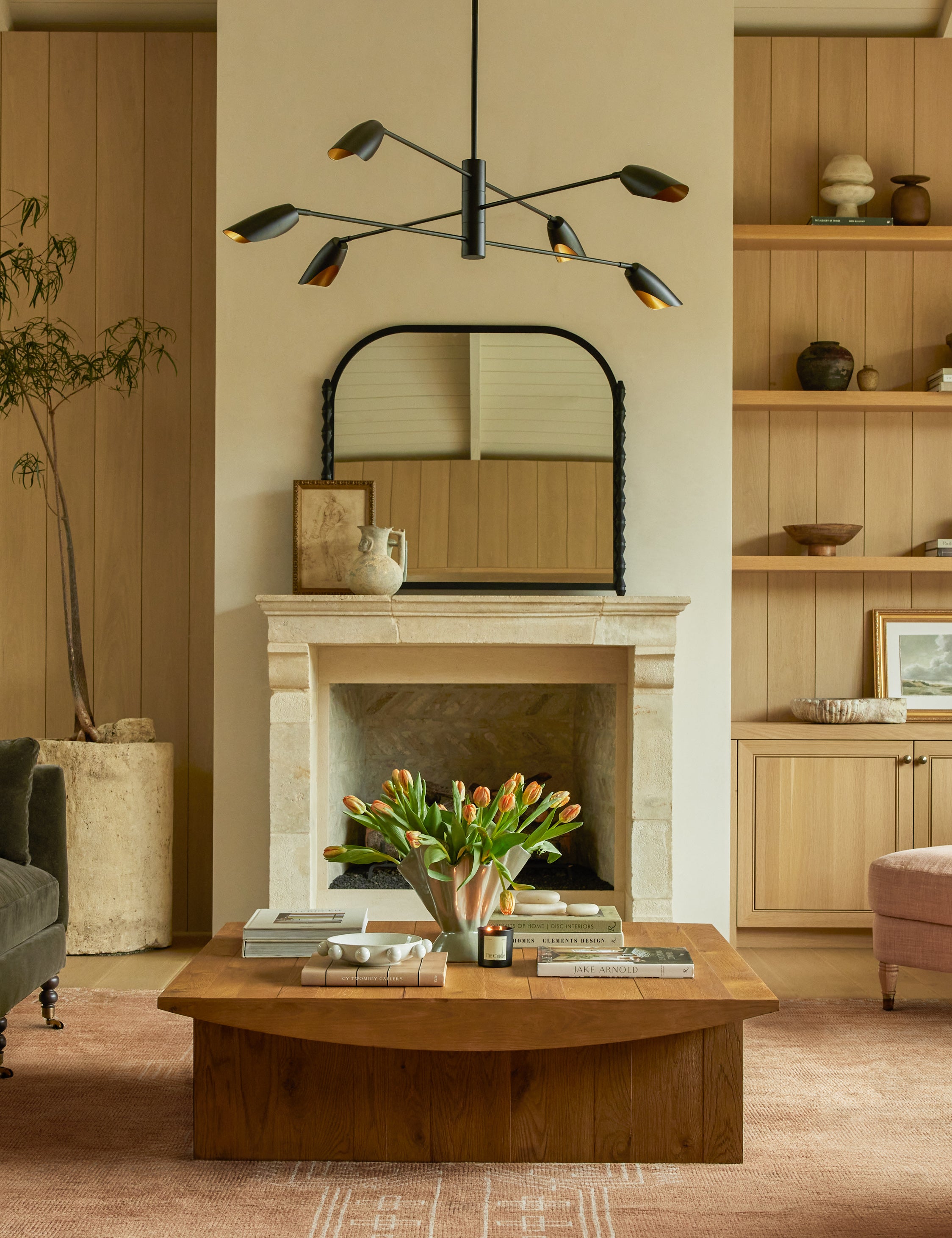 Topia arched carved wood mantel mirror by Ginny Macdonald in black hung above a fireplace in a livingroom.