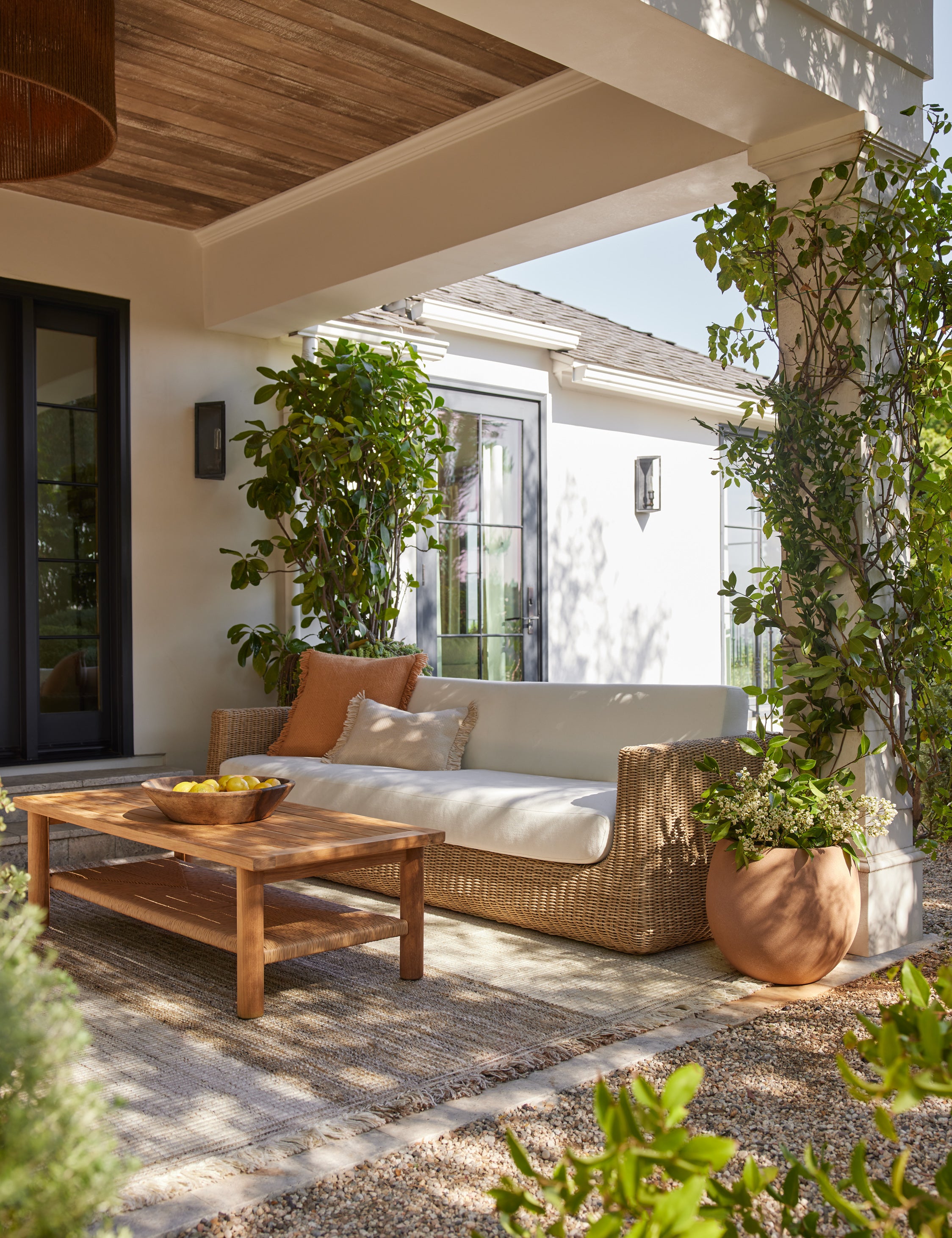 Aisha wide arm modern wicker outdoor sofa styled with a teak outdoor coffee table on a covered patio.