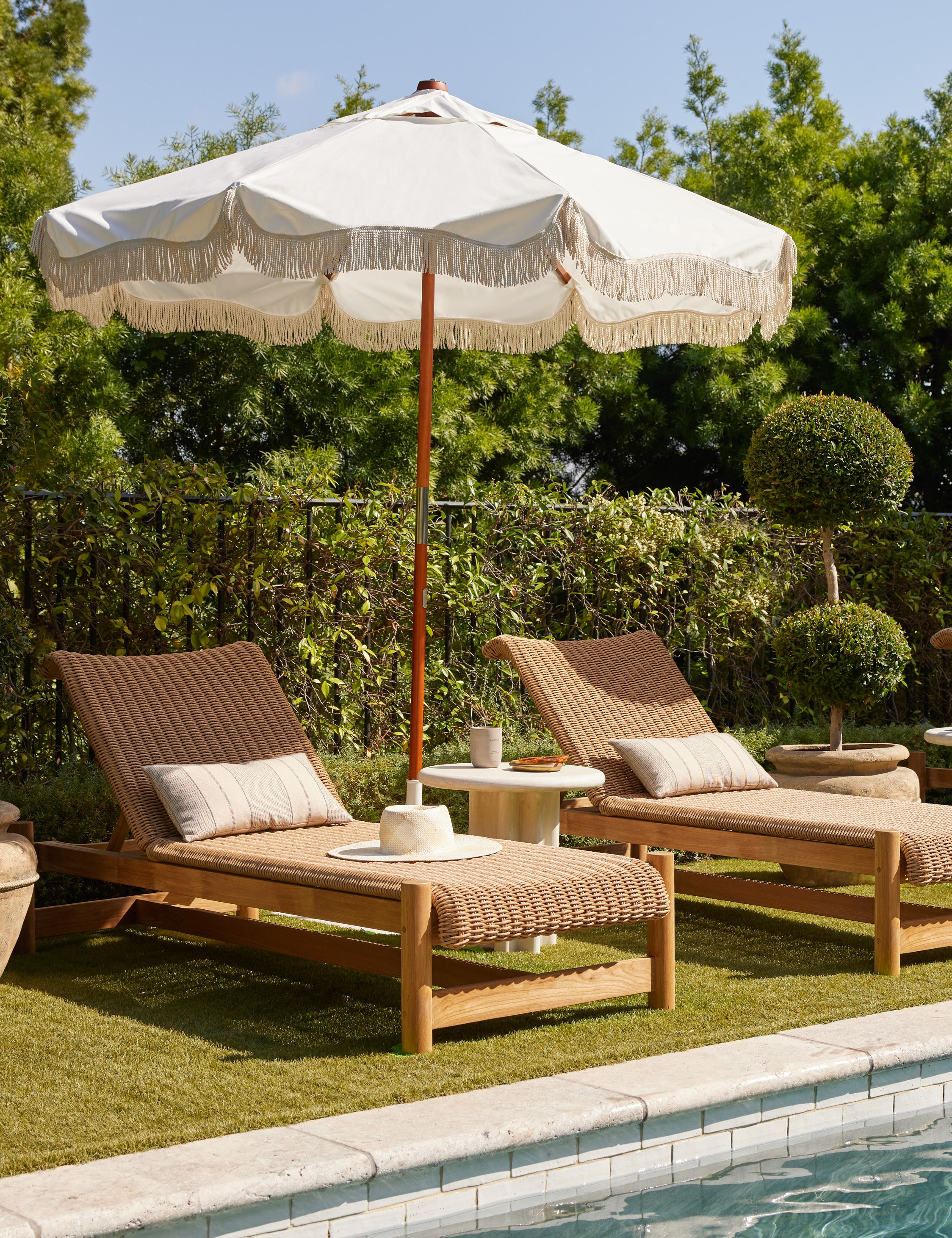 Two Gally wicker and teak outdoor chaise and umbrella by the poolside.