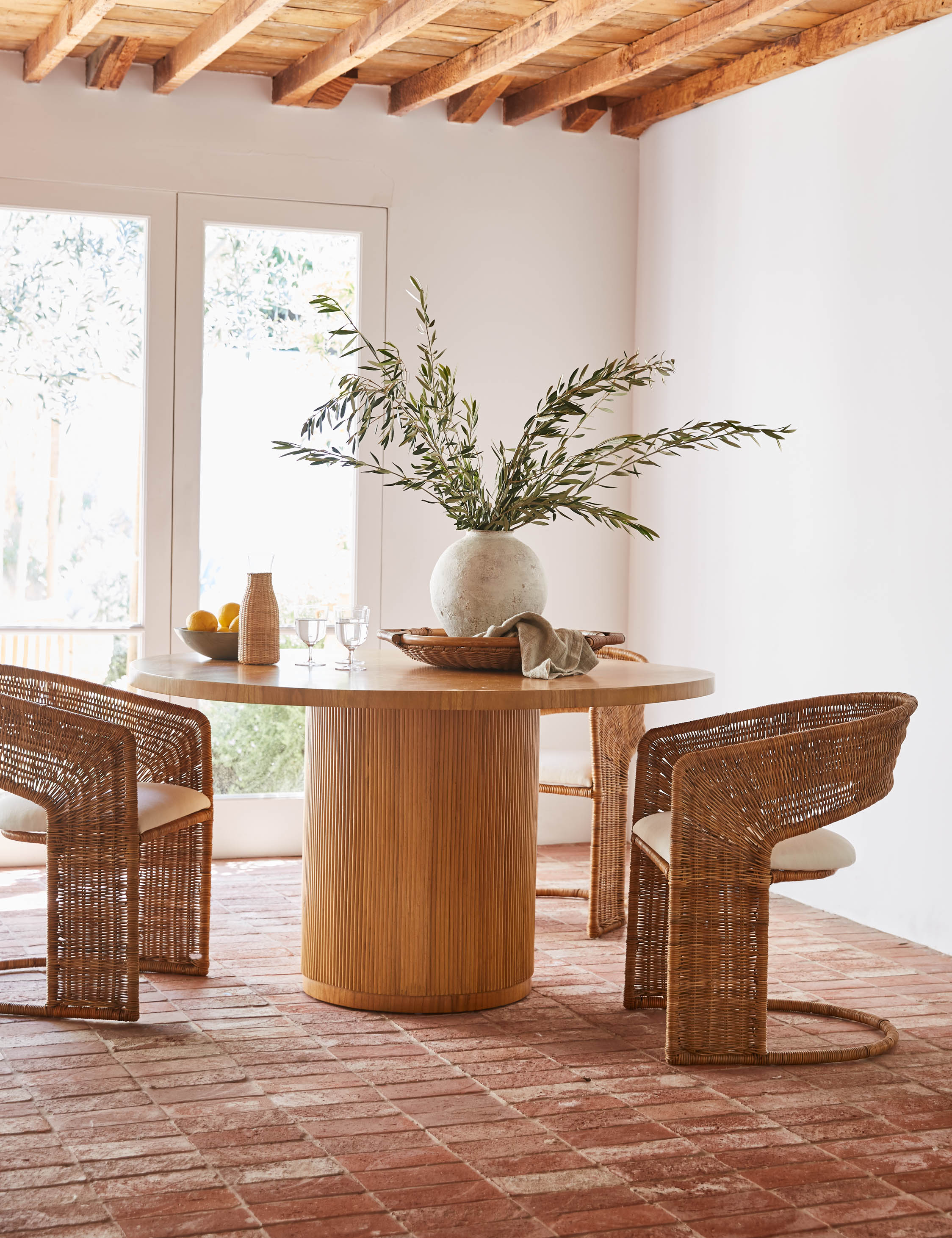 Elvia round rattan stacked leg dining table styled with rattan barrel back dining chairs.
