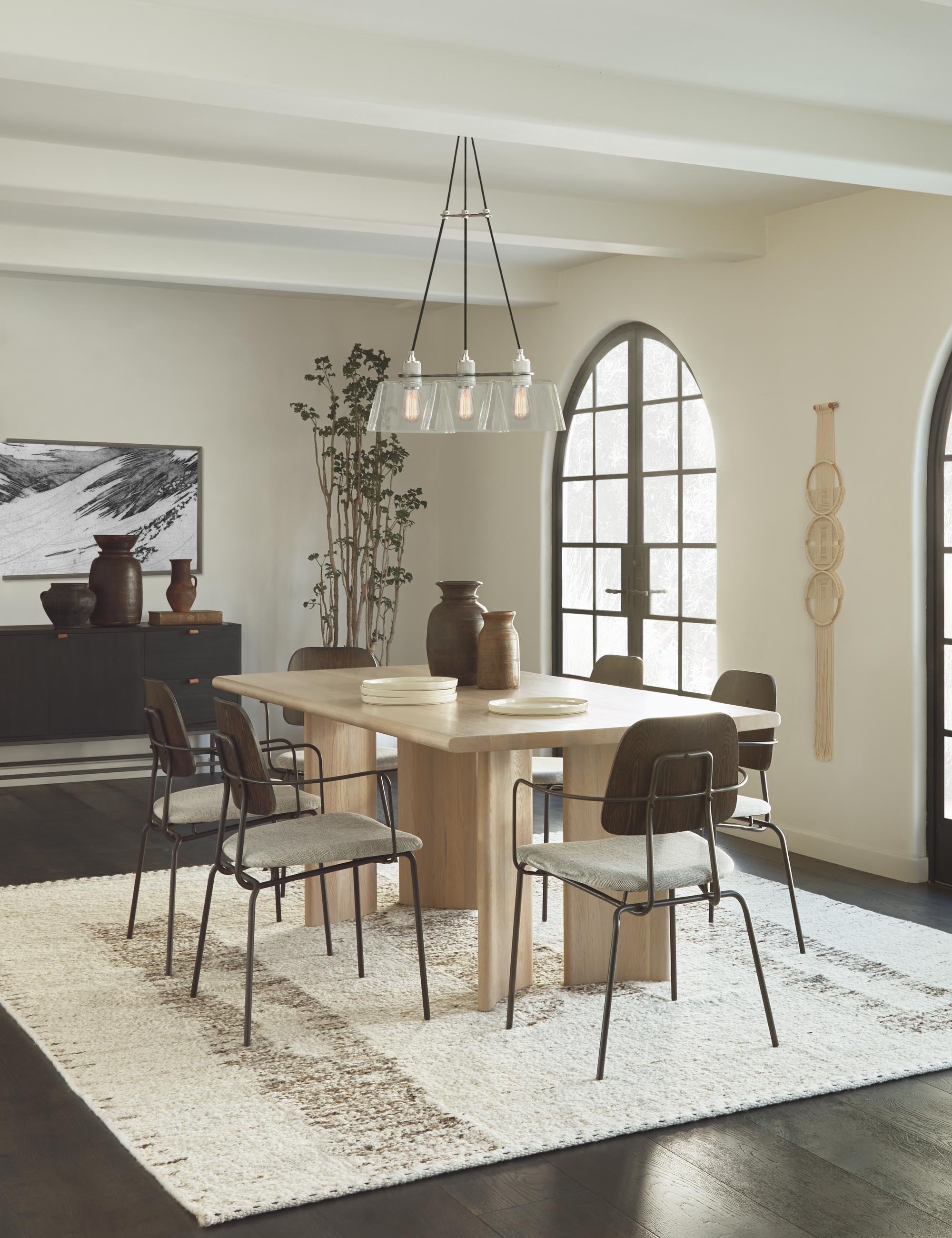 The esha rug lays in a dining ruun under six iron-framed dining chairs, a rectangular wooden dining table, and a glass chandelier
