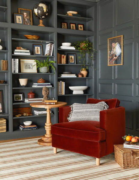 #showall::39655448608867 | The Belmont paprika red velvet accent chair sits atop a striped rug in front of a gray wall with a built-in shelf and decor