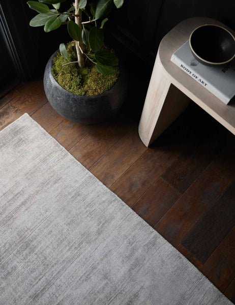 #color::gray #size::6--x-9- #size::8--x-10- #size::9--x-12- #size::10--x-14- #size::12--x-15- | Close up view of the gray dylan rug laying next to a gray stone planter and a light wood sideboard