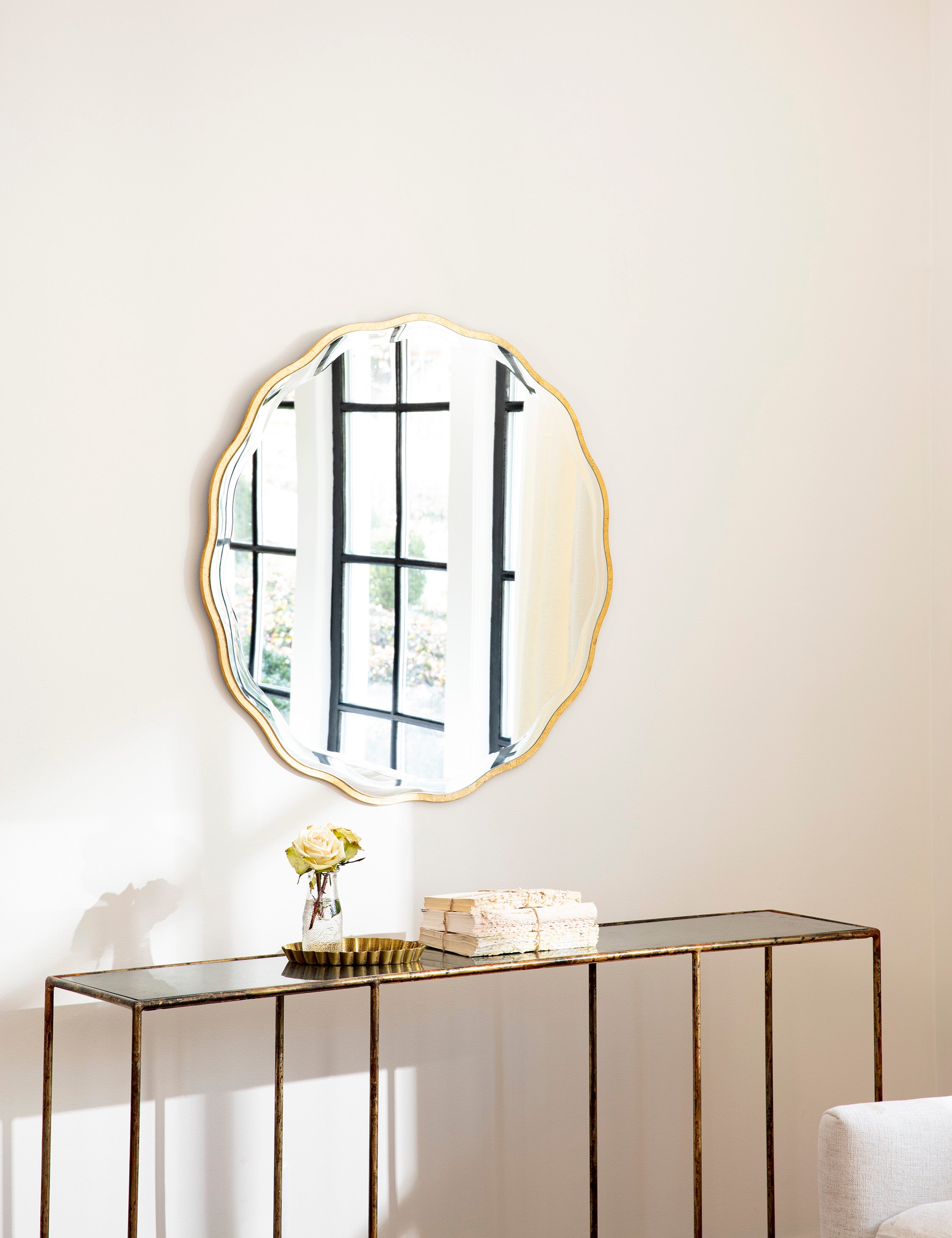Angled view of the scalloped gold beveled edge Candice Round Mirror by Regina Andrew hanging on the wall above a console table.