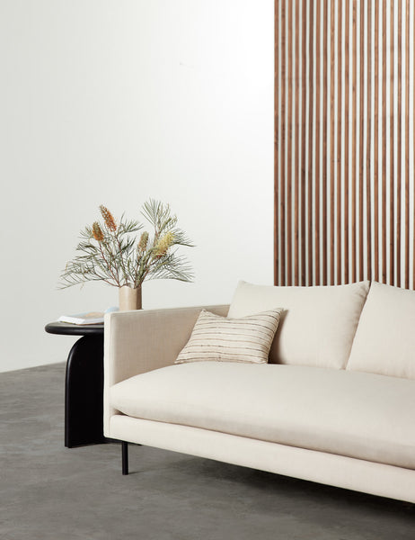 #size::12--x-20- | Marit neutral lumbar silk pillow with striated lines sits on a natural linen couch in a room with a black side table