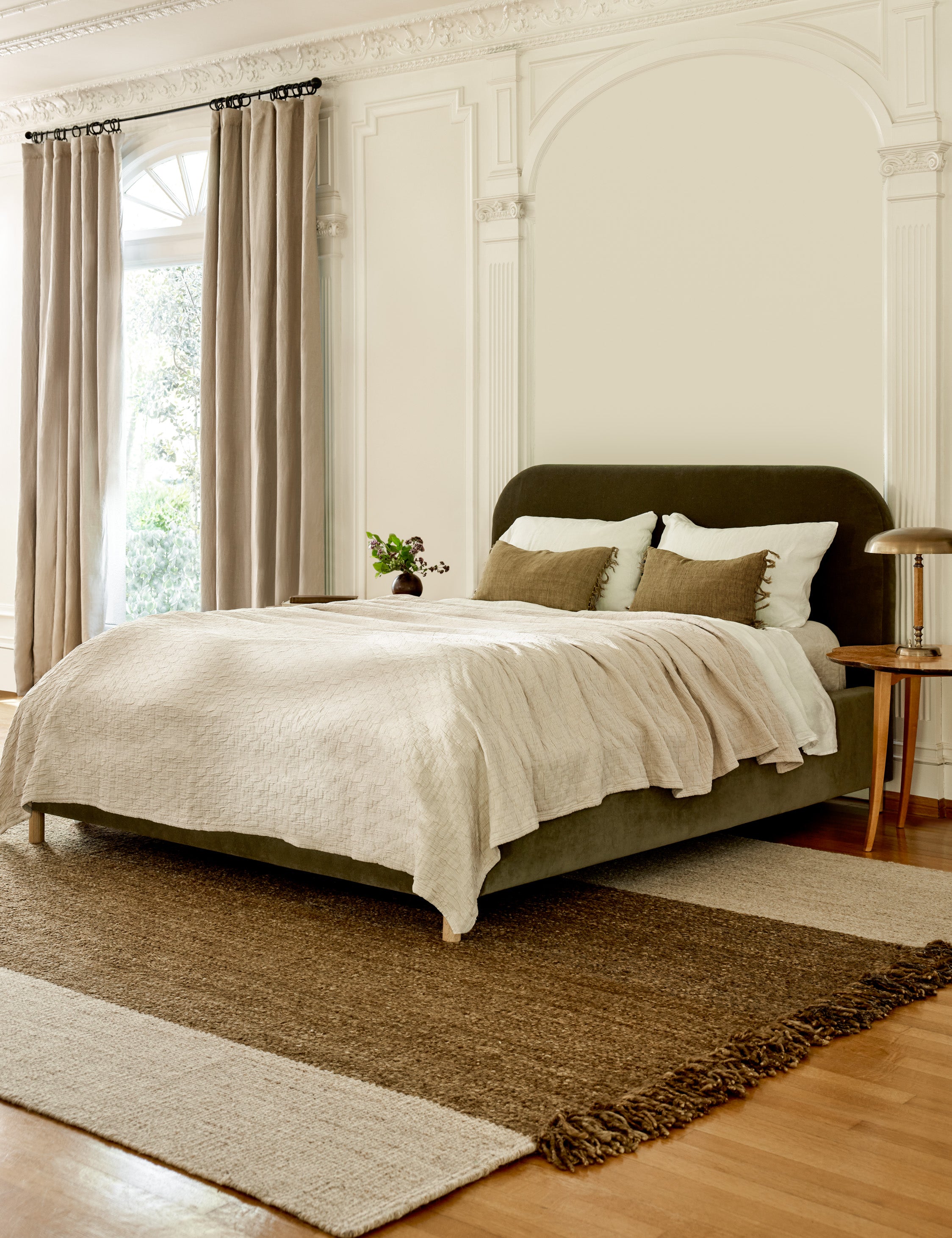  The Solene Loden Velvet platform bed sits atop a brown and natural rug in a room with a tall ceiling and accented walls