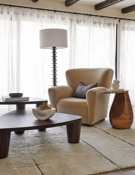 #color::ebony | The Fishbone black ebony Floor Lamp by Regina Andrew with a gradated wooden base and linen drum shade sits in a living room with nested coffee tables, a beige velvet accent chair, and a wooden textured side table