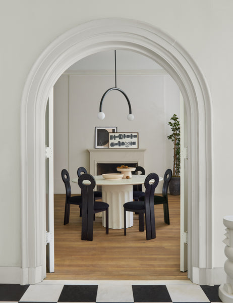| The Doric white round dining table sits in a dining room surrounded by black wooden sculptural chairs