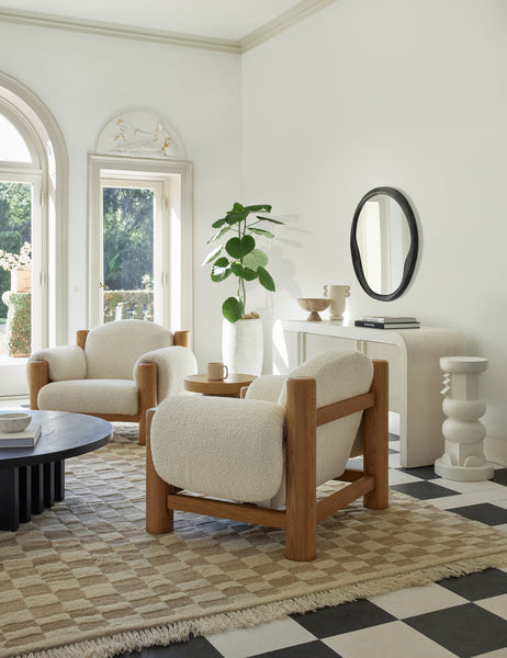 | Two James faux sherpa accent chairs sit atop a natural and ivory checkerboard rug in a room with high ceilings and white walls