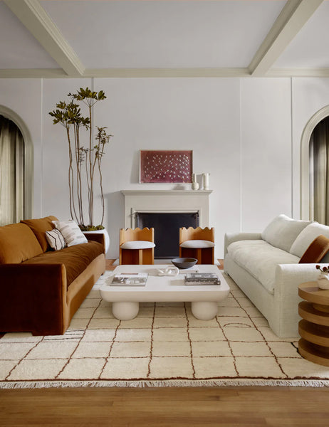color::ivory #size::6--x-9- #size::8--x-10- #size::9--x-12- #size::10--x-14- #size::12--x-15- | Ivory and ochre Irregular Grid Rug by Sarah Sherman Samuel lays in a living room in between a cognac velvet and linen sofa with a rounded coffee table in the middle
