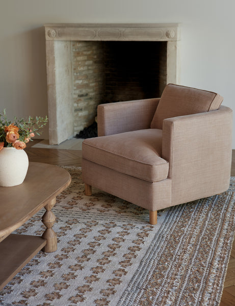 #showall::40199323320419 | The Belmont apricot linen accent chair sits atop a gray and neutral-toned rug in front of a wooden framed fireplace 