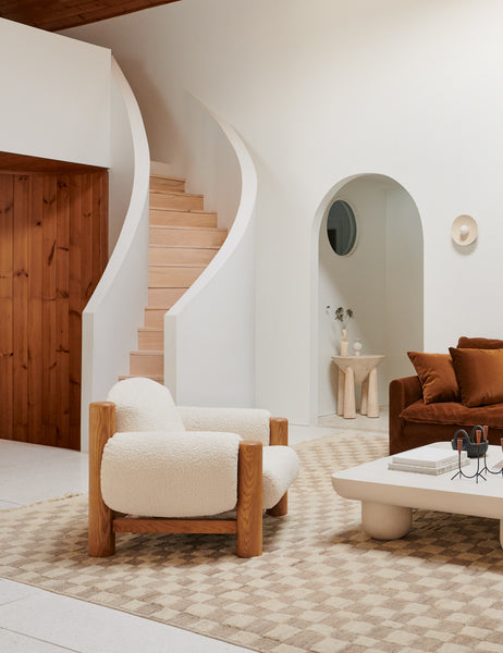 | The James faux sherpa accent chair sits atop and natural and ivory rug in front of a natural wooden curved staircase