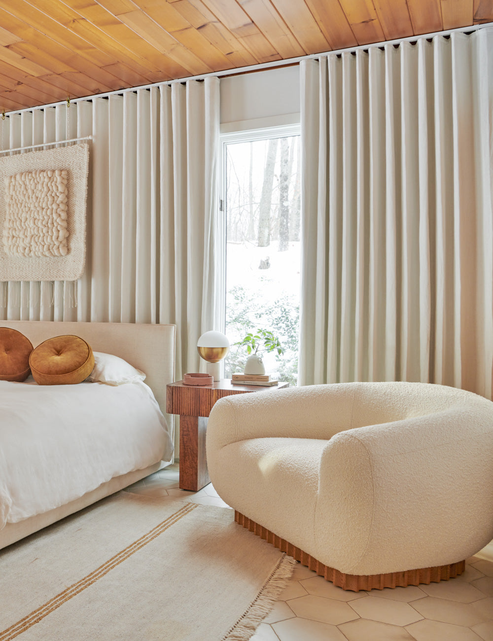 The Billow ivory boucle lounge chair sits next to a natural linen framed bed atop a hexagonal tile floor