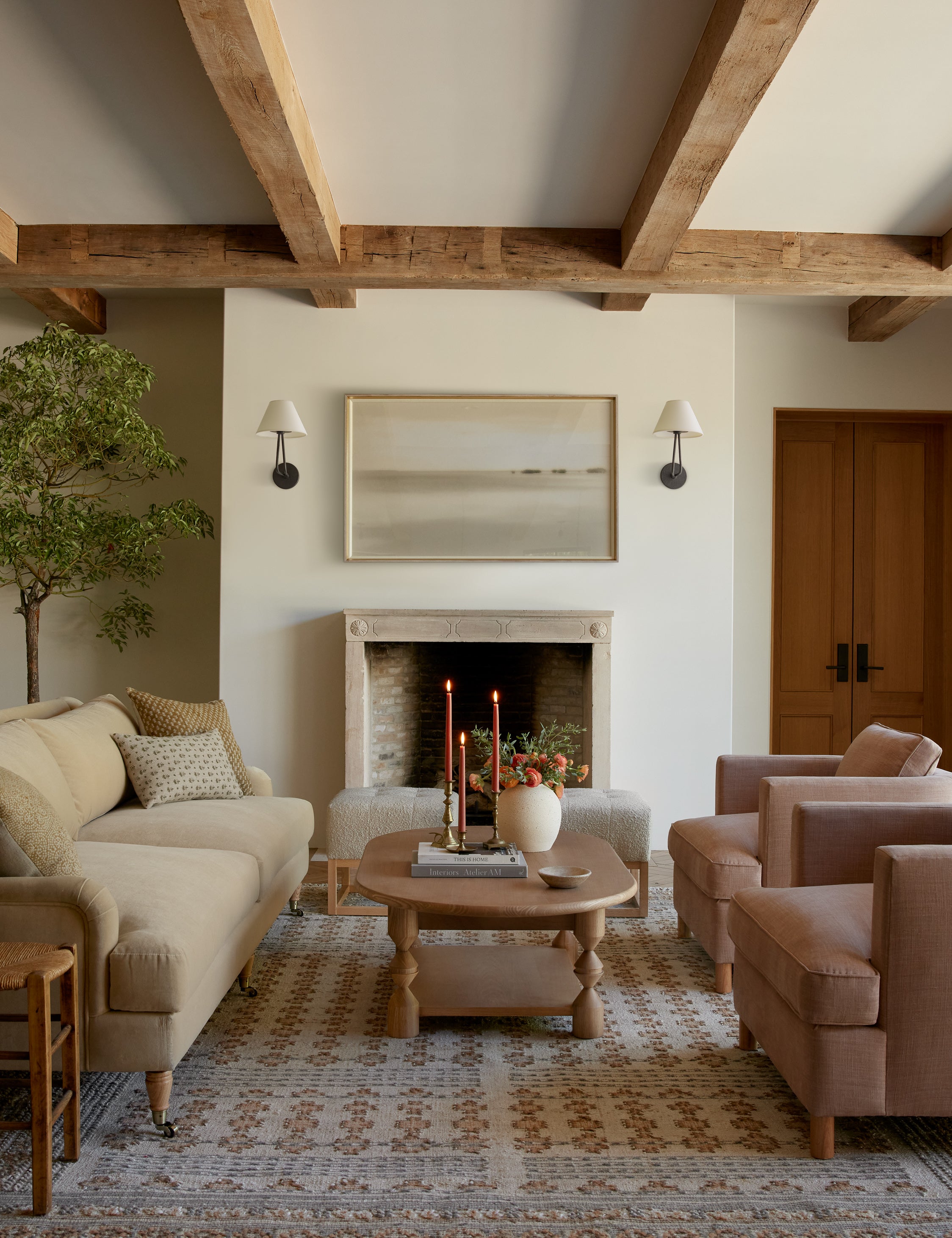  Two Hayden double-armed black sconce lights hang on both sides of a landscape painting in a living room with warm-toned furniture
