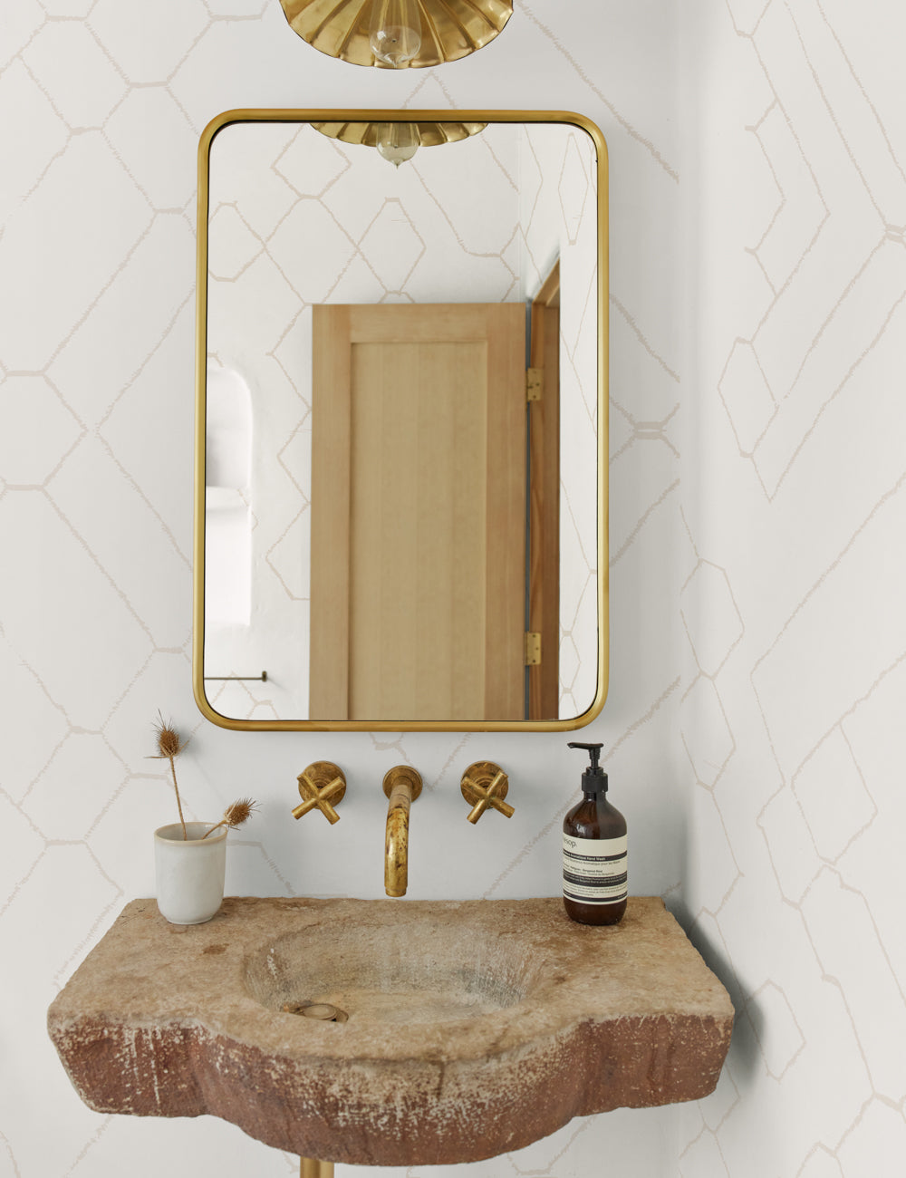 The Moroccan beige and ivory Wallpaper Mural by Sarah Sherman Samuel is in a bathroom with a wooden sink and a rectangular golden framed mirror with rounded edges.