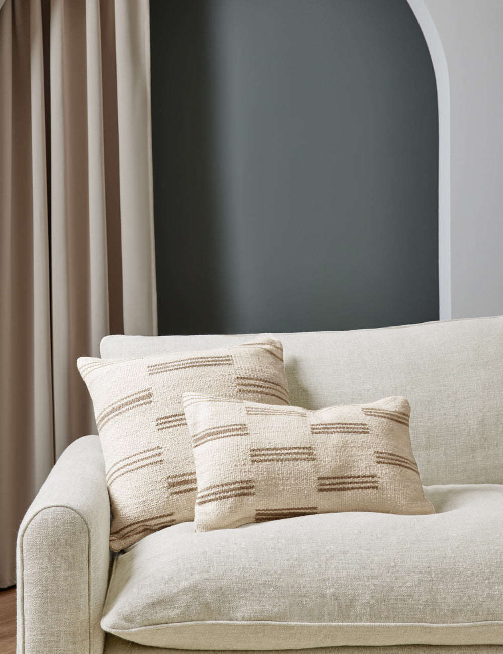 Two Stripe break natural and cream pillows by Sarah Sherman Samuel sit together atop a natural linen sofa in a room with green painted walls