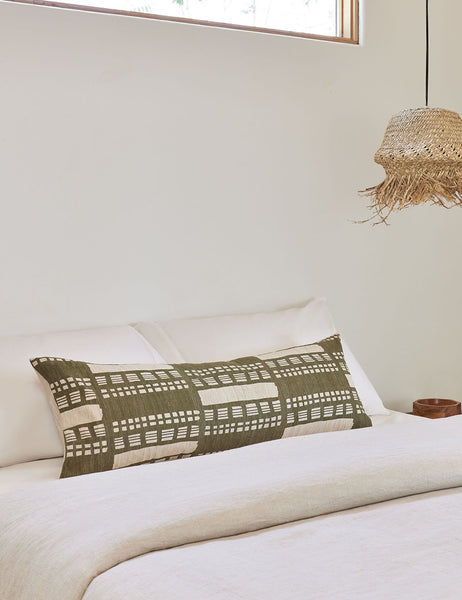 #size::14--x-40- | Stonewalk green geometric long lumbar throw pillow by Élan Byrd lays on a bed with natural toned linens to the left of a jute pendant light