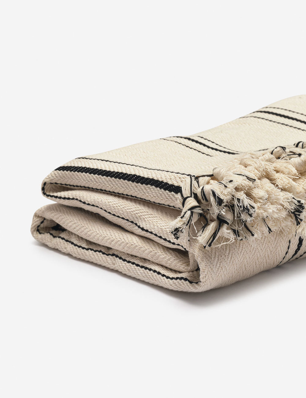 Angled-view of the Monte viso natural and black striped bed cover with fringed ends by House No. 23