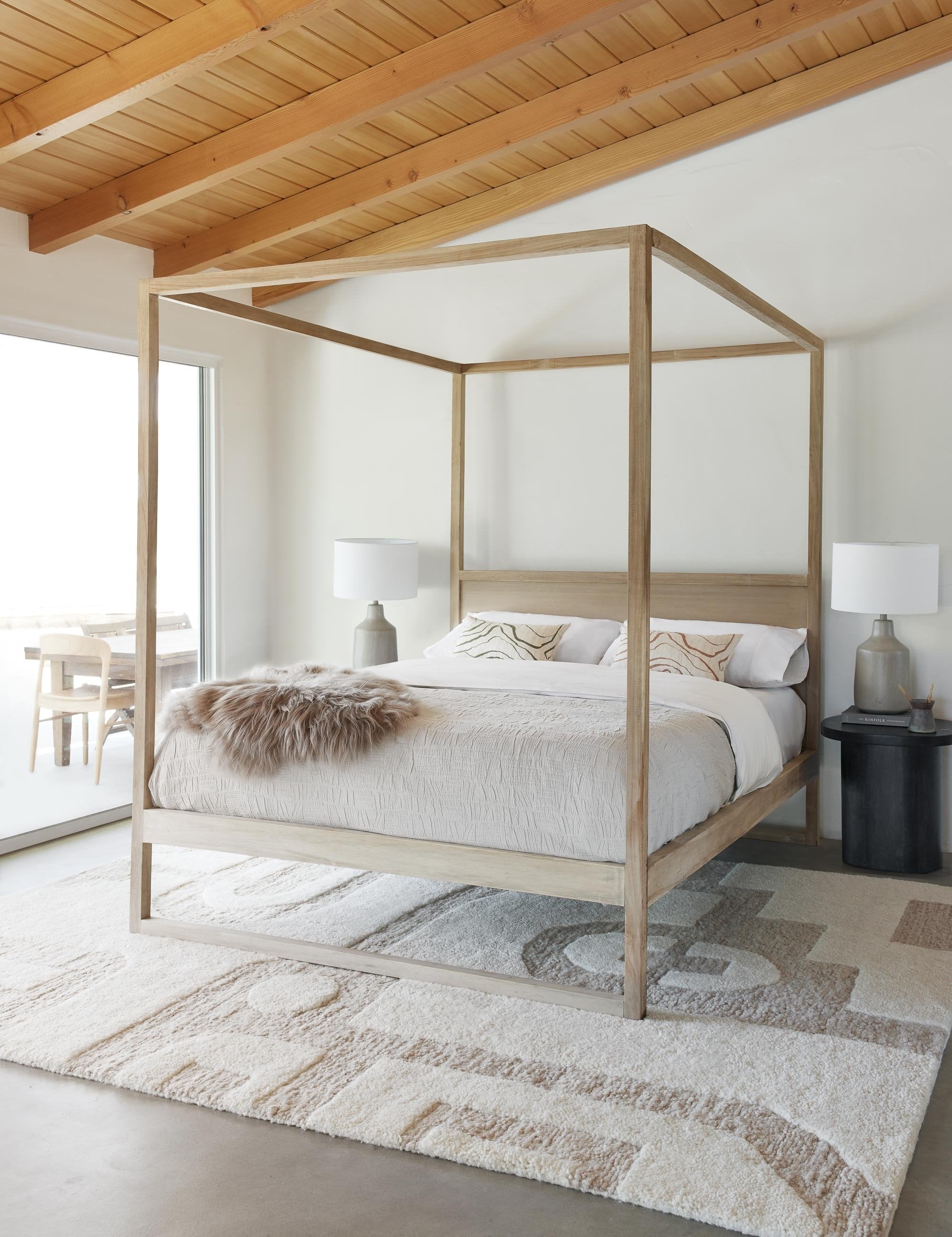 Canyon Olive Green Lumbar Pillow sits on a wooden canopy bed in a room with a cream and neutral geometric rug and a wooden ceiling
