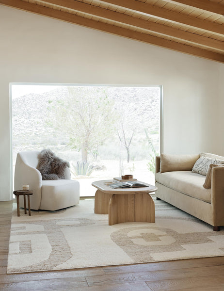 #size::6--x-9- #size::8--x-10- #size::9--x-12- #size::10--x-14- #size::12--x-15- | The Oasis plush geometric neutral-toned rug by Élan Byrd lays in a living room with an oval wooden coffee table, a white linen accent chair, and a light brown velvet sofa
