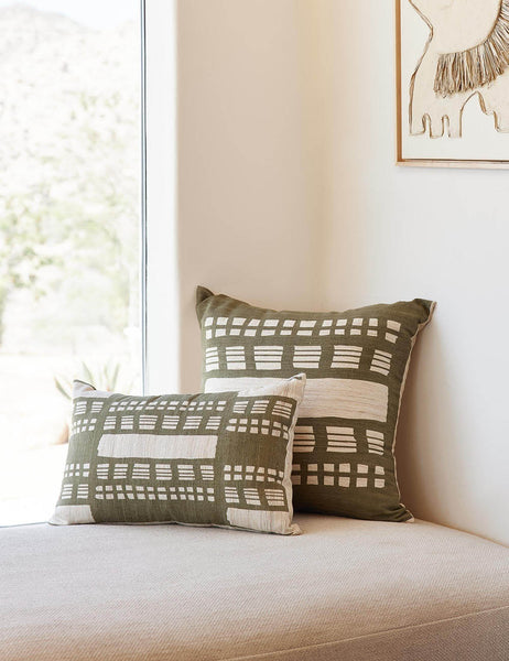 #size::20--x-20- | The Stonewalk green geometric throw pillow by Élan Byrd sits on a natural linen cushioned bench in front of a large window