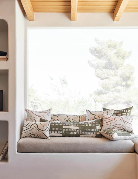 #size::20--x-20- | The Stonewalk green geometric throw pillow by Élan Byrd sits on a natural linen cushioned bench with other terracotta and green toned throw pillows in front of a large window