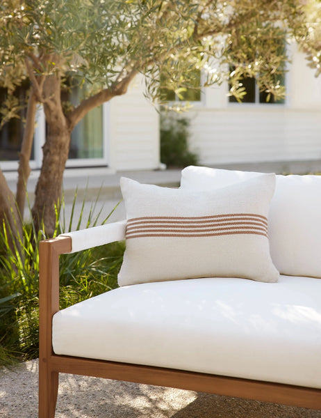 #color::rust-stripe #style::lumbar | Katya Indoor and Outdoor lumbar cream Pillow with rust brown stripes in the center sits on a white cushioned sofa in an outdoor space