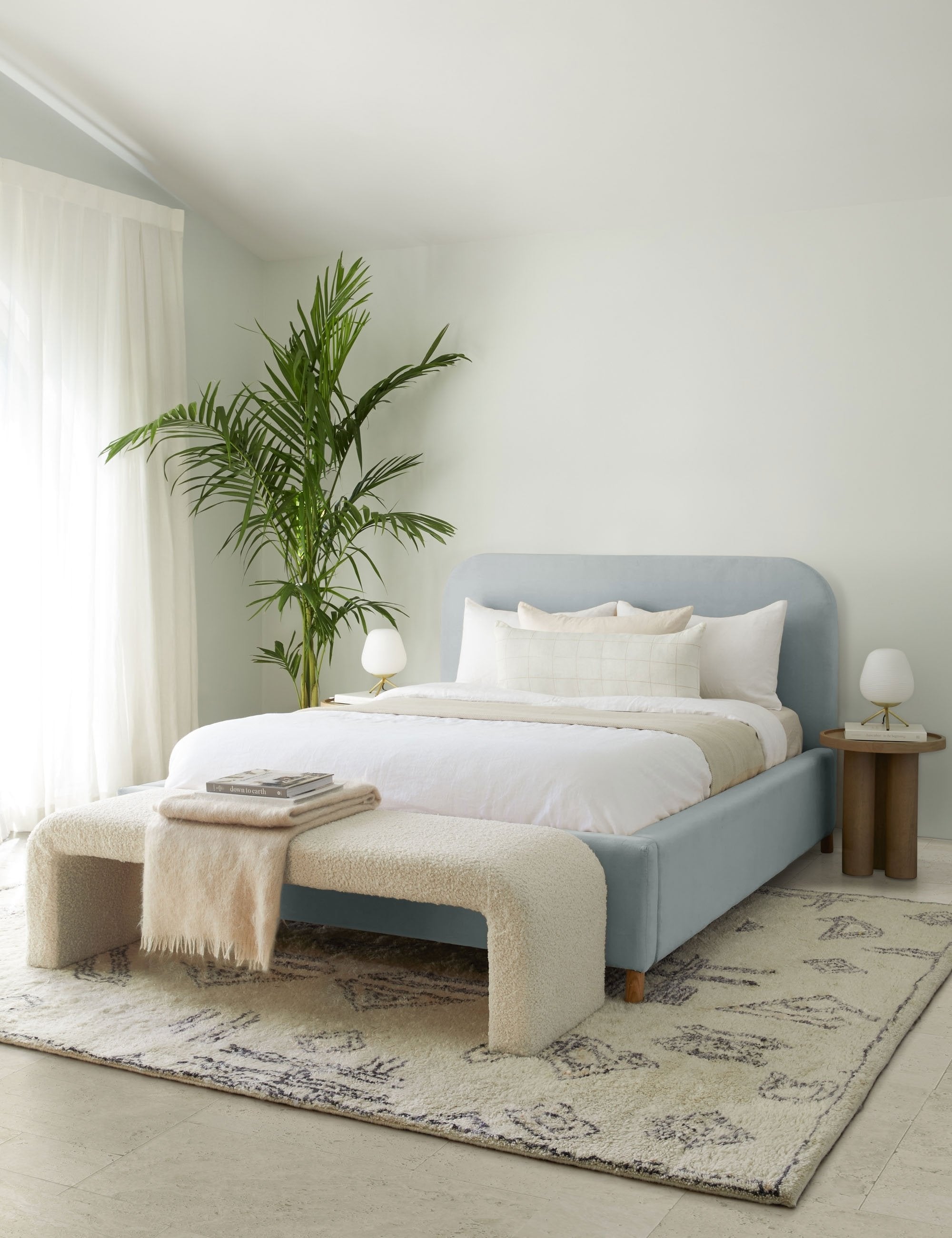  The Solene dove light blue velvet platform bed sits atop a plush patterned rug with a boucle cream bench and white linens