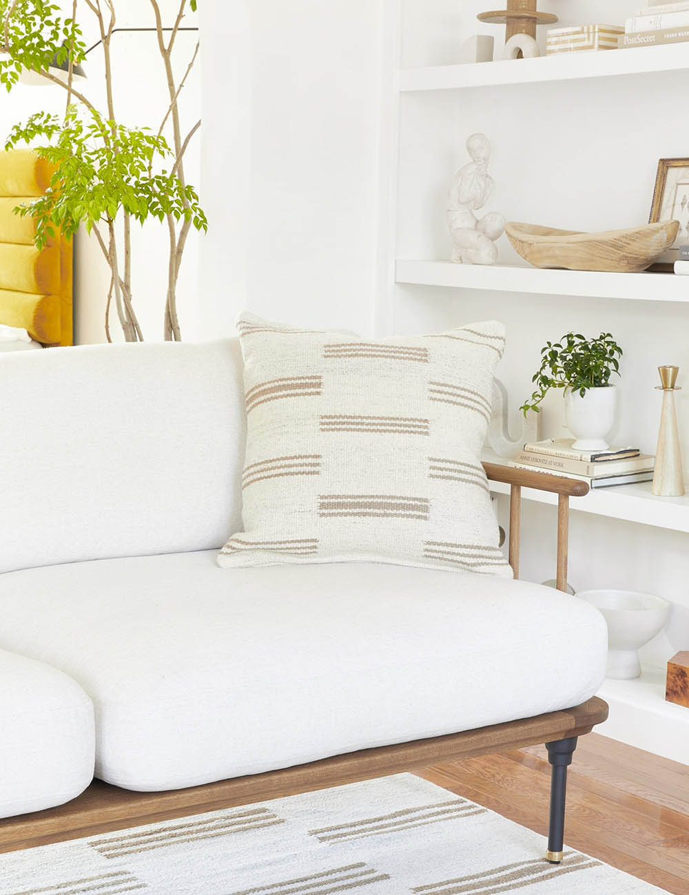 Stripe break natural and cream square pillow by Sarah Sherman Samuel sits on a white couch in a living room with a stripe break carpet
